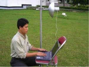 Gunadi with a Wokbolik connected to his computer. The Wokbolik is made out of a regular USB wireless adapter, a three-inch PVC pipe, and a regular cooking wok