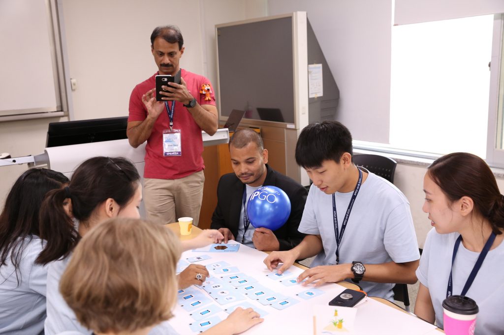 A photograph of APNIC's Sunni Chendi with a group of students playing IPGO at APIGA 2018.